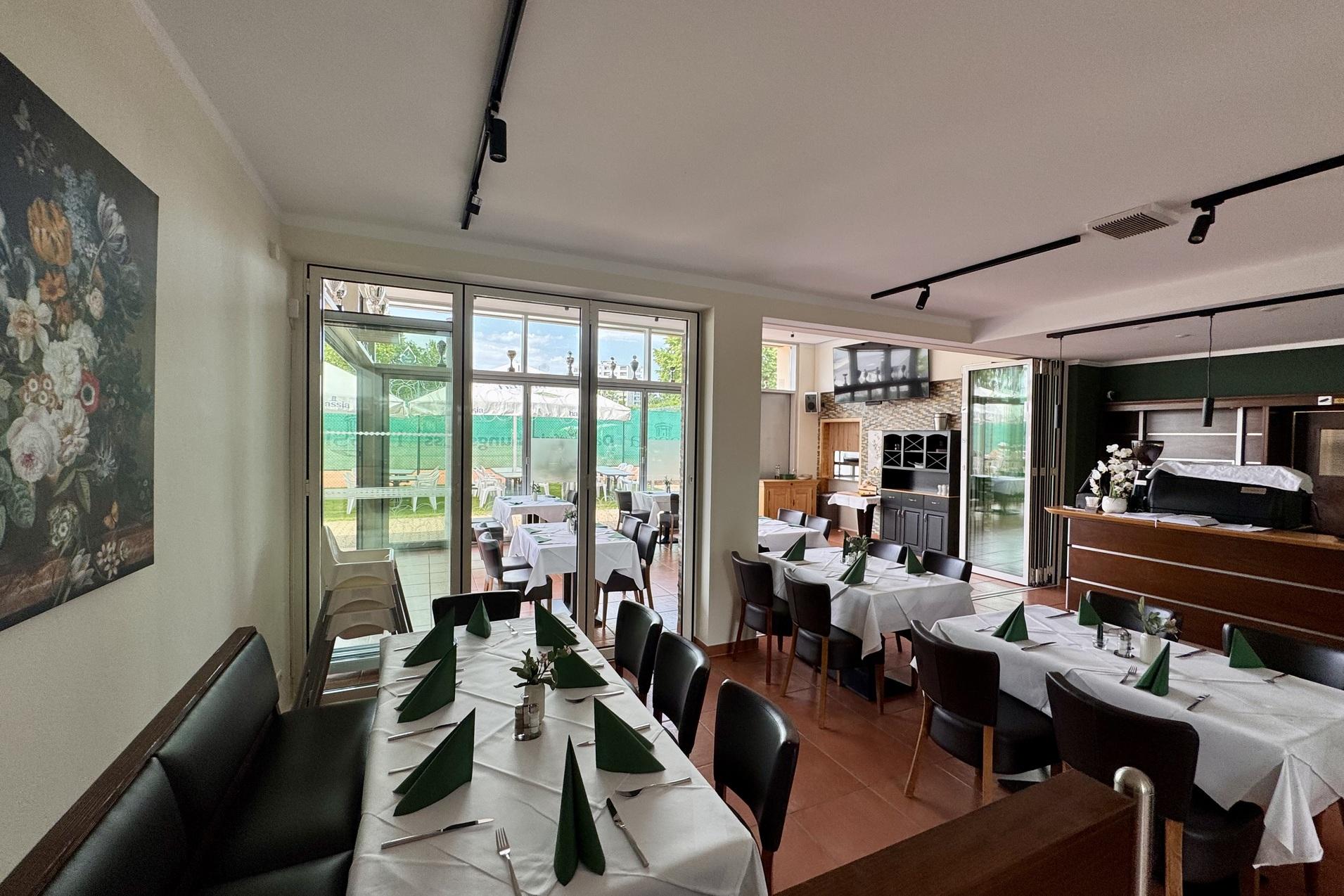 Gemütlicher Restaurantbereich mit Tischen, gedeckt mit weißen Tischdecken und grünen Servietten, daneben Fenster mit Ausblick.
